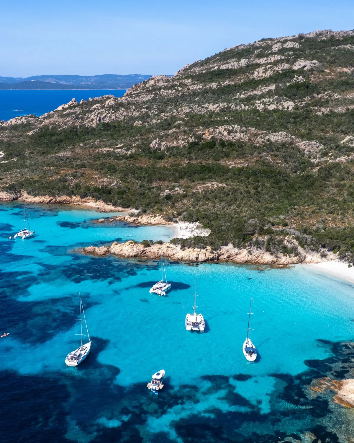 Costa granitica sarda con acque turchesi e barche a vela all'ancora